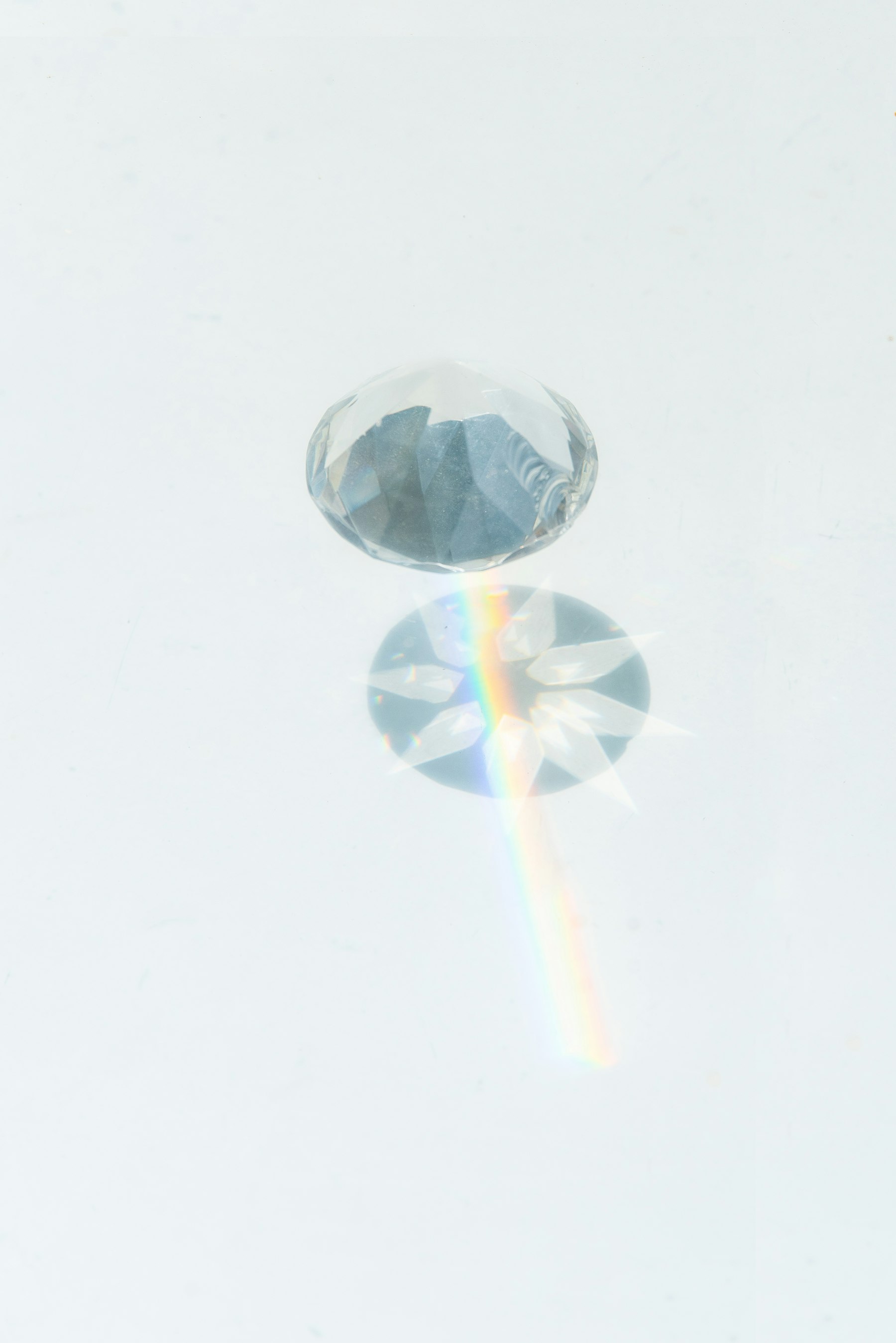A cut crystal on a pale surface splitting light into a thin rainbow