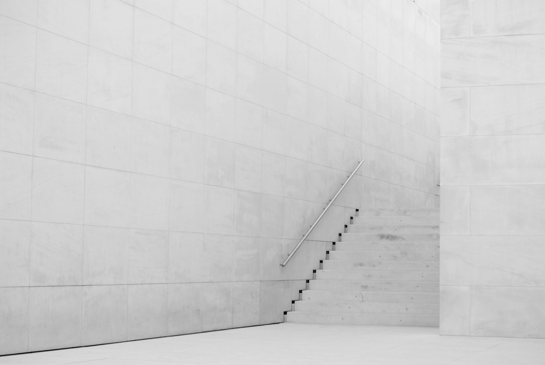 A clean white concrete staircase with a single handrail against a pale wall